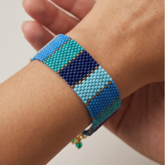 Close-up of a Dailot blue and turquoise striped beaded bracelet with gold-tone accents worn on a wrist.