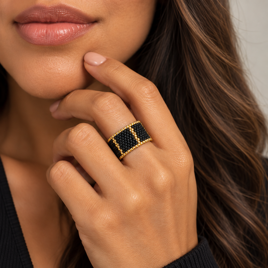 Linear black and gold-tone Miyuki Delica ring worn on a model showing its wide geometric design