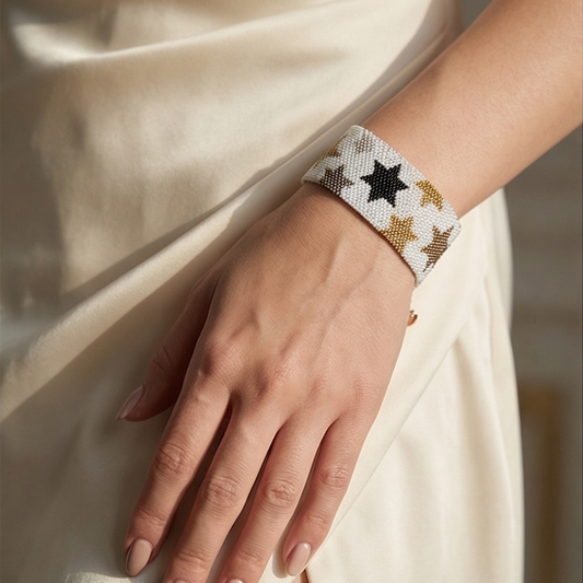 Close-up of a Dailot white beaded bracelet with black and metallic stars worn on a wrist against an ivory dress.
