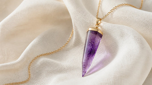 Amethyst pendulum necklace with a gold chain on soft ivory fabric