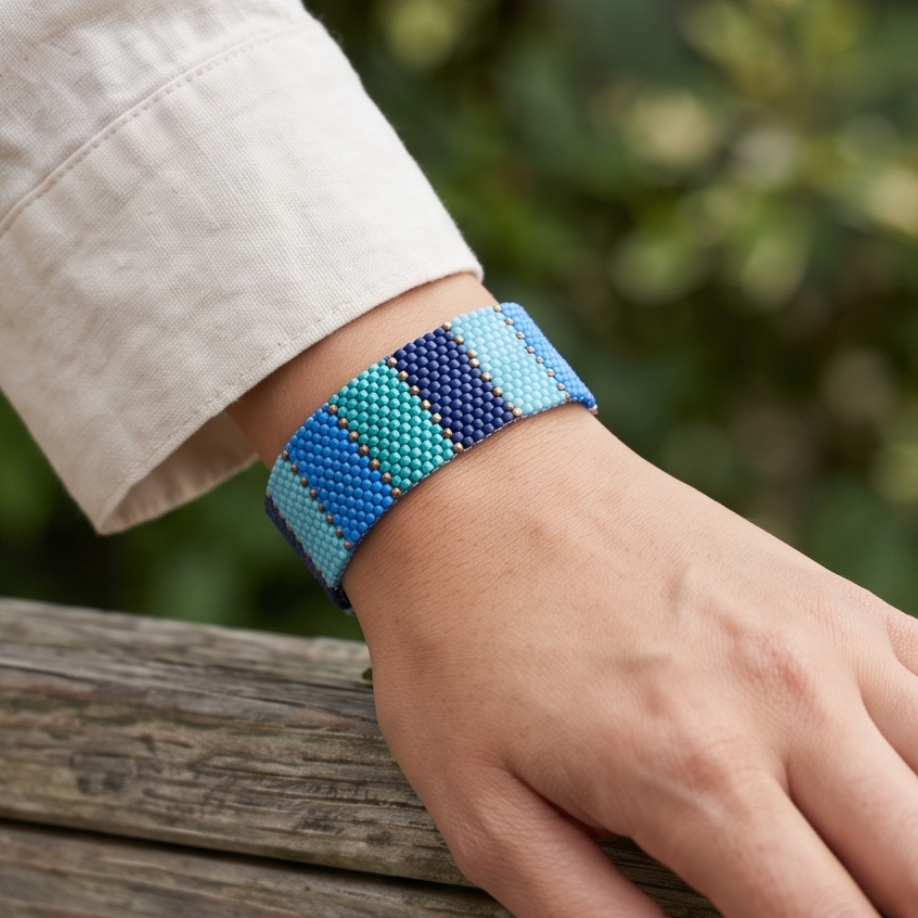 Dailot blue and turquoise beaded bracelet worn with a white sleeve, with the hand resting on a wooden railing outdoors.