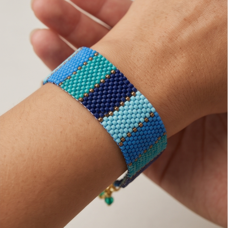 Close-up of a Dailot blue and turquoise striped beaded bracelet with gold-tone accents worn on a wrist.