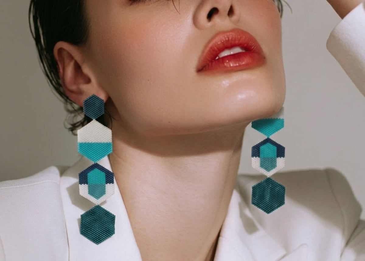 Model wearing a white blazer and long geometric beaded dangle earrings in turquoise, white, and navy blue