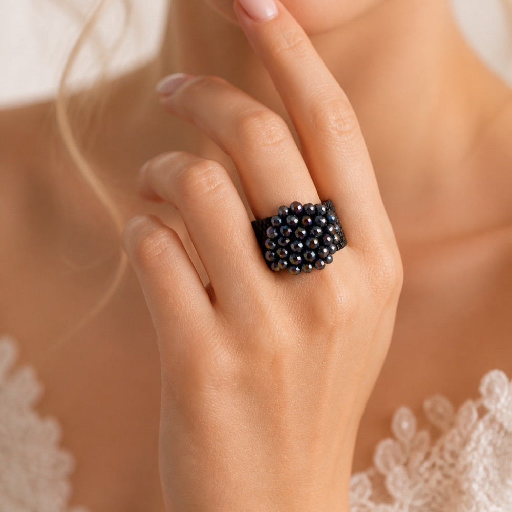 Close-up of a wide black beaded ring with multicolored faceted beads on a beige display surface.