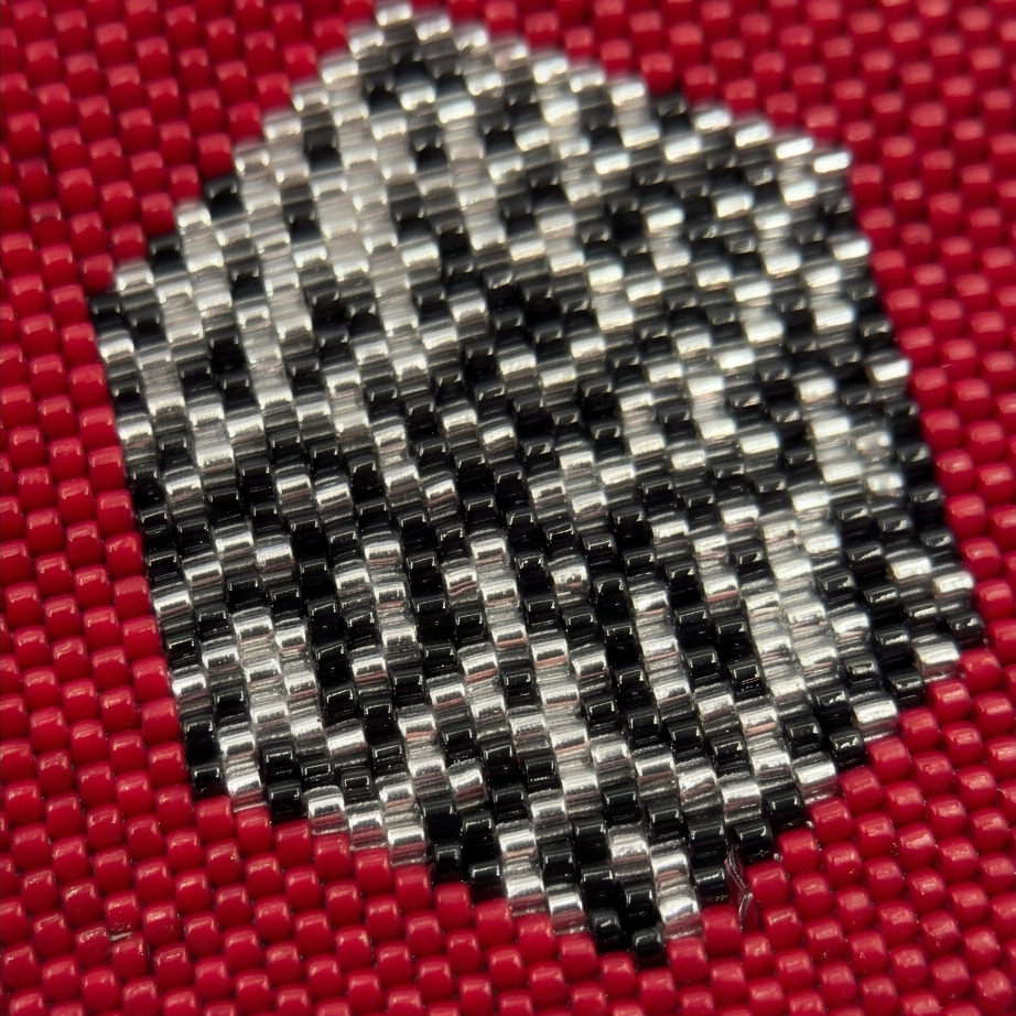 Close-up of red earring beadwork framing a geometric pattern in black and silver-tone beads.