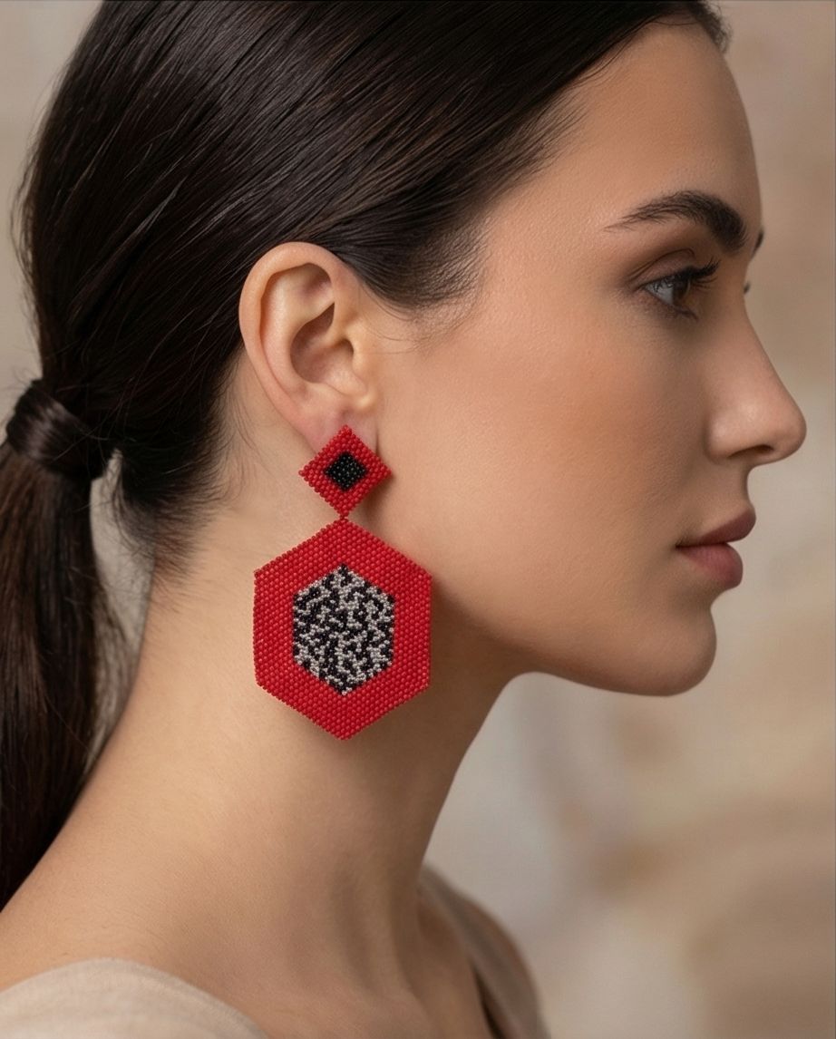 Side profile of a model wearing a red geometric beaded earring with a diamond top and black and silver-tone hexagonal center.
