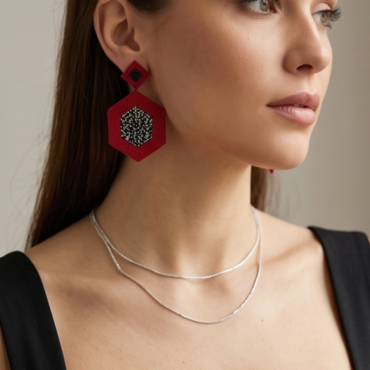 Model wearing red geometric beaded drop earrings with black and silver-tone details, styled with a black top.